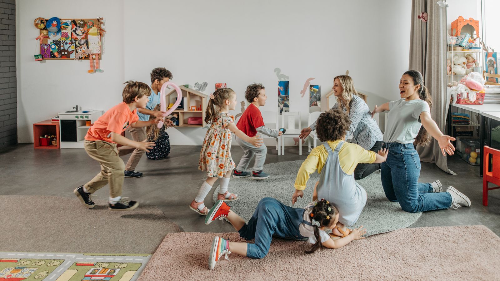 Childcare professionals playing with a group of young children in a bright, well-equipped care room